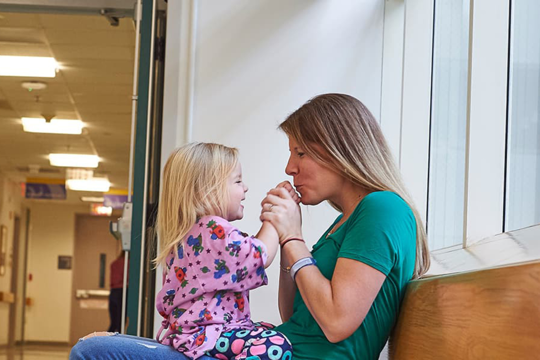 Mother sitting in hospital hallway, playing with daughter sitting on her lap
