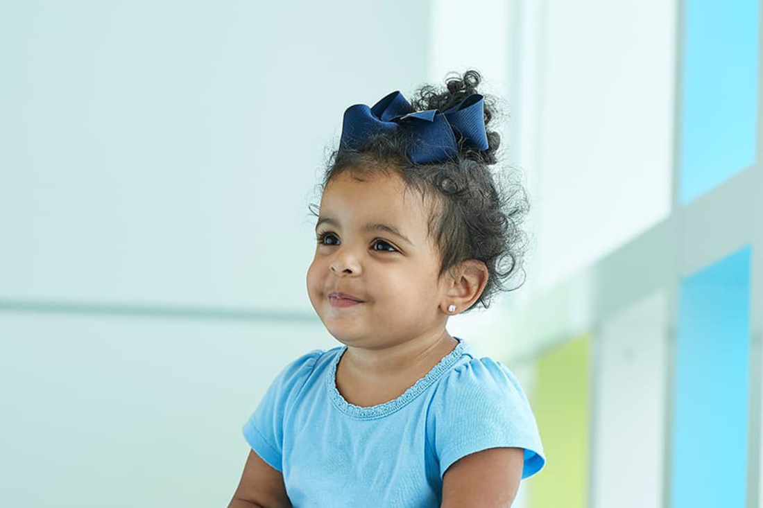 Toddler with blue shirt and blue bow in her hair looks to the side.