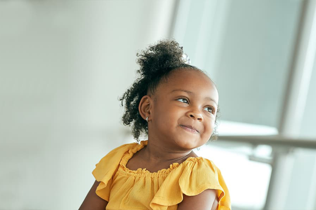 Little African American girl with yellow shirt looks to the side and smiles.