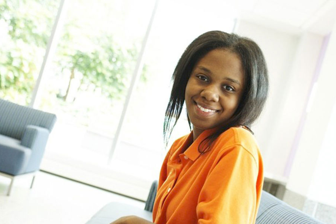 Young adult woman wearing orange shirt smiling at the camera.