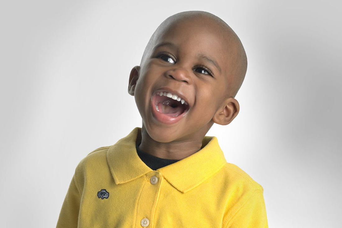 Little boy wearing yellow polo smiling big at the camera.