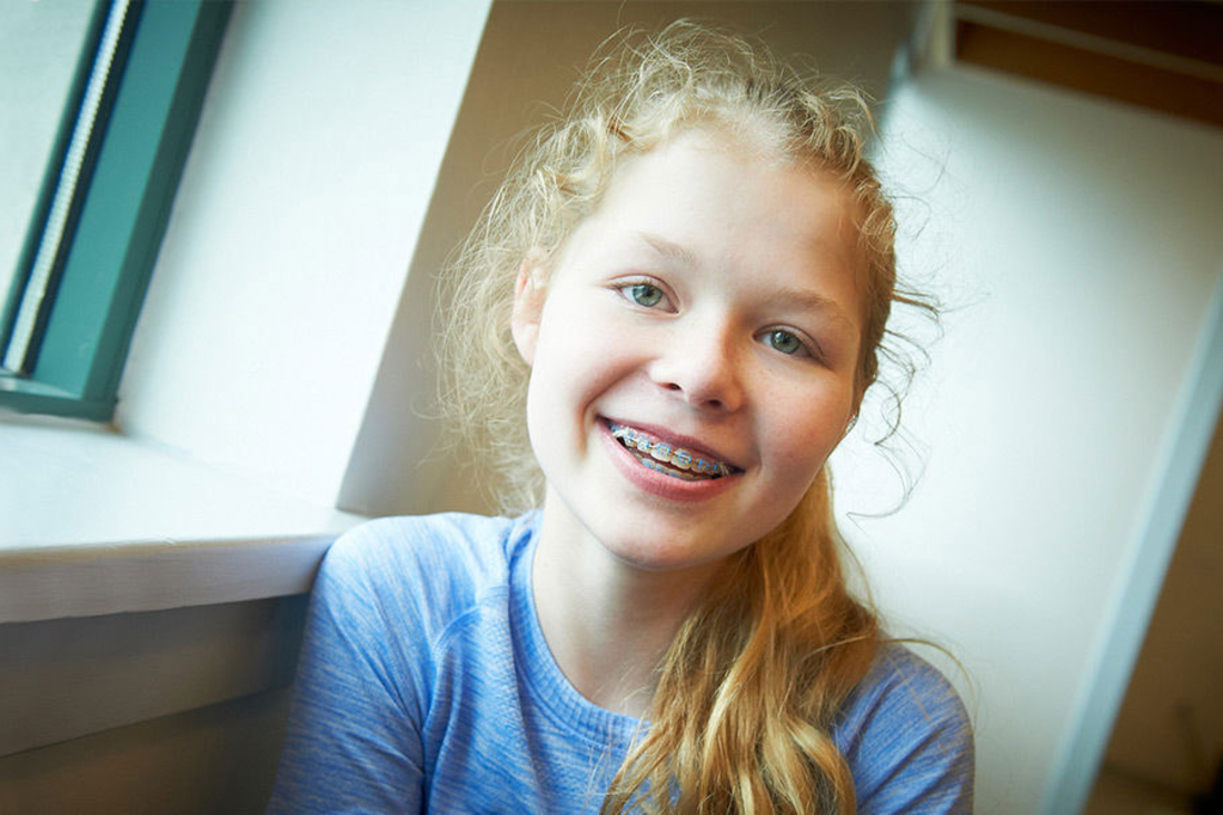 Girl with a curly blonde ponytail and braces smiles at camera.