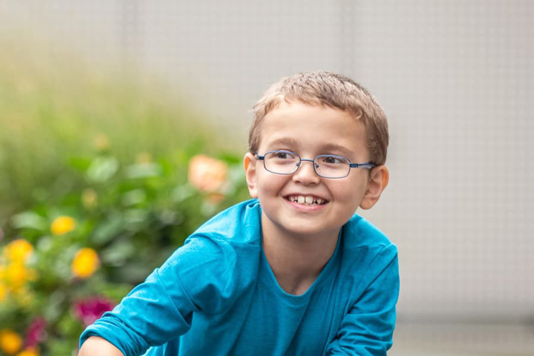 Young boy with glasses and teal shirt smiling.