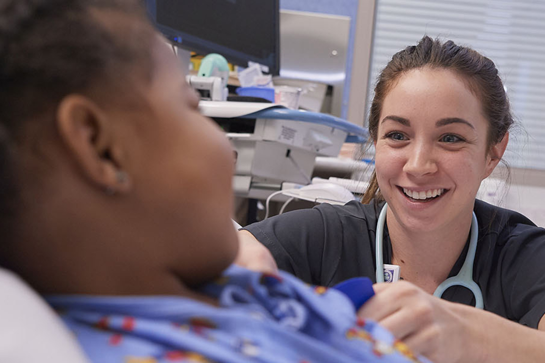Nurse sitting next to patient bed talking to patient.