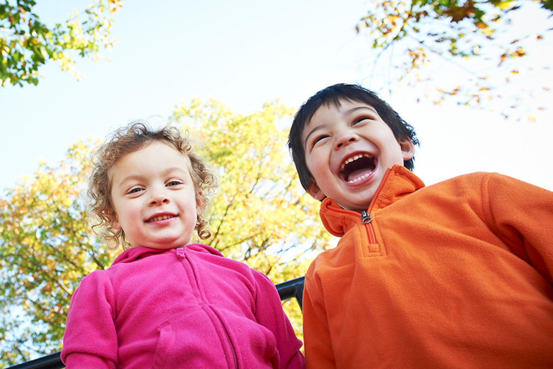Boy with orange sweatshirt and girl with pink sweatshirt look towards the camera and smile.