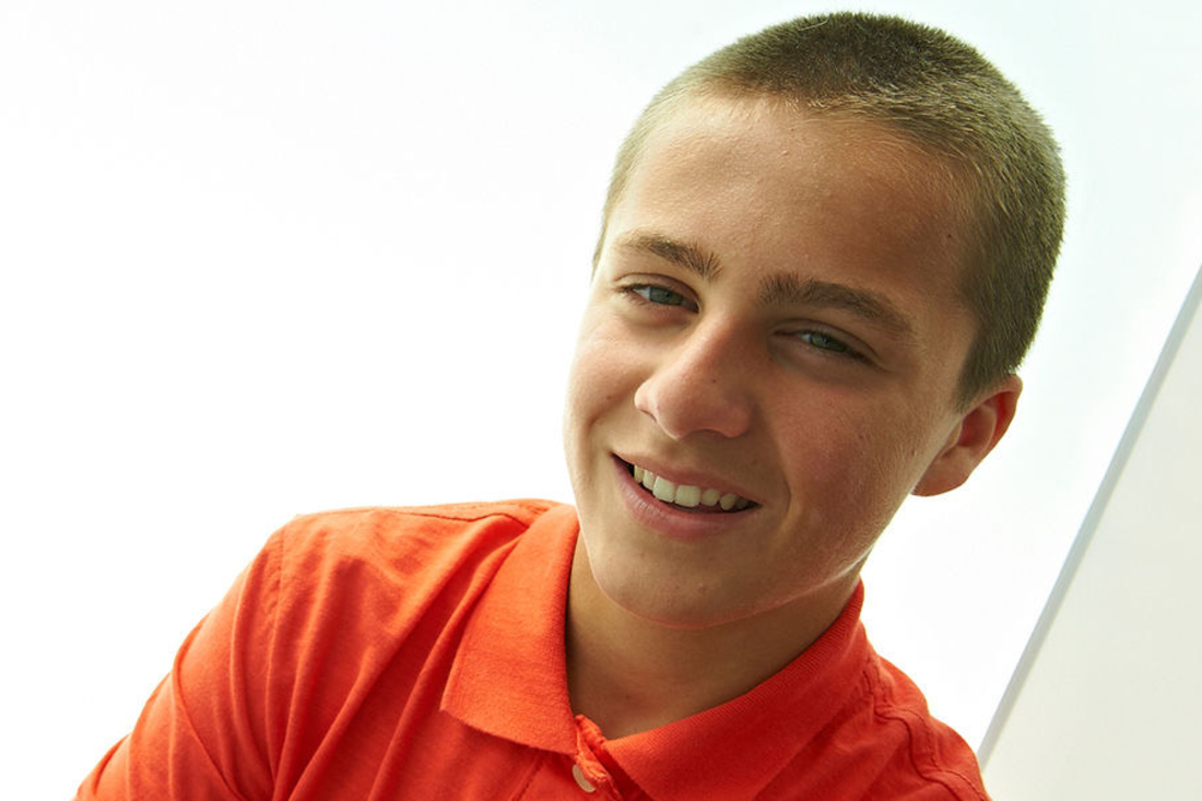 Teen boy wearing orange polo smiles at the camera.