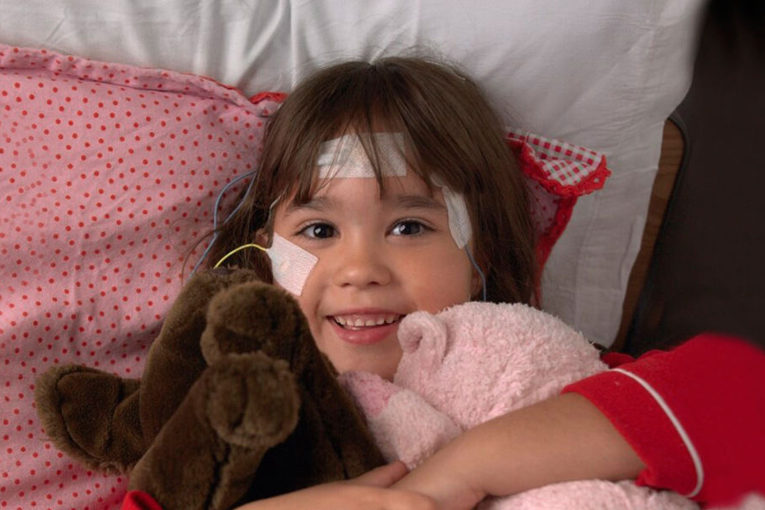 Young girl smiling in bed, hugging stuffed animals
