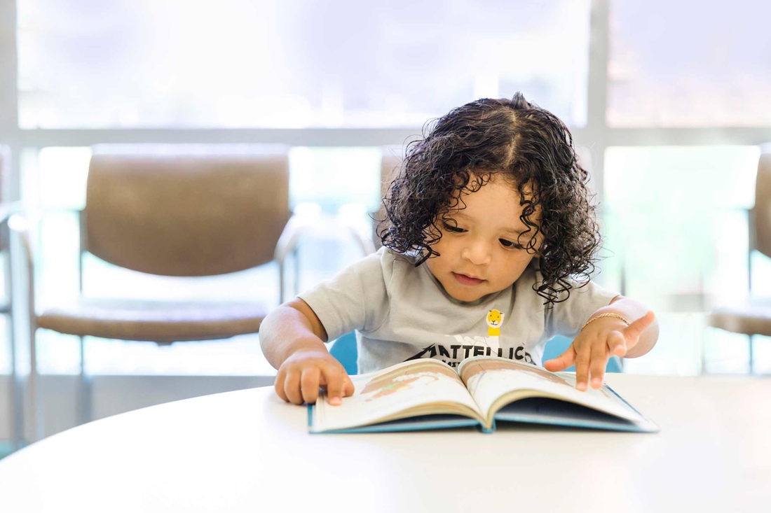 Toddler reading a book at a table.