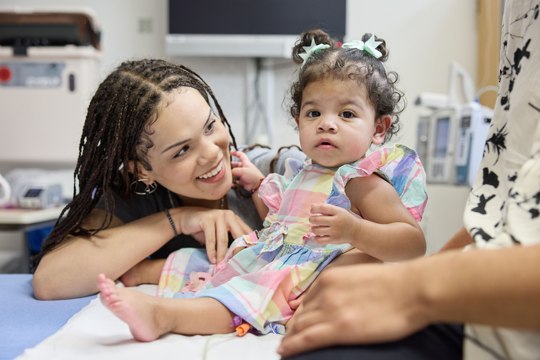Mom smiling and looking at her little girl on exam table.
