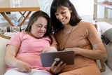 Mother and kid smiling at a tablet.
