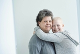 Teen girl cancer survivor with her mother on plain wall.