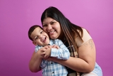 mom smiling and hugging her boy with a purple background behing them.
