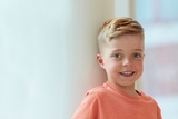 Blonde and green-eyed boy smiling while leaning against the wall.