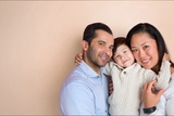 Family of three smiling and looking grateful on peach background.