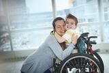 Happy boy patient hugging his smiling mother in wheelchair at hospital.