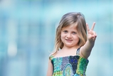 Young girl in dress with cleft lip holding up peace sign with finger.