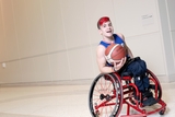 Smiling teen boy with fun haircut in red wheelchair holding basketball.