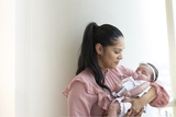 Mom with infant daughter who is wearing a pink bow and is sleeping and sucking a pacifier.