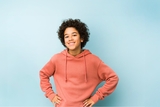 Teenager smiling with hands on their hips, wearing a coral sweatshirt.