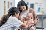 Doctor listening to heart and giving exam to baby sitting on her mothers lap.