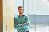Staff member with folded arms leaning on a wooden wall
