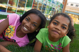 Two girls lay in the grass smiling at the camera.