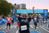 Woman smiling and holding her arms up at the finish line of the Parkway Run & Walk