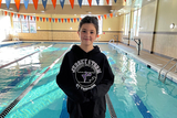 School aged girl smiling in front of an indoor lap pool