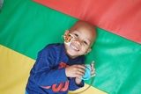 Boy receiving with cancer laying on a colorful background and smiling