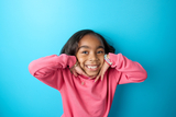 Girl in pink sweatshirt on blue background framing her face with hands and smiling
