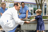 Little girl born in the SDU stands in garden with providers who cared for her.