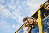 Smiling school age girls lean out of school bus windows