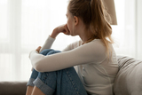 young depressed teen siting in couch looking out window