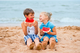 Two kids on the beach eating watermelon