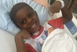 Khymir flexing his arms and smiling in hospital bed