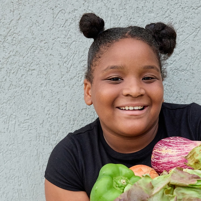 young girl smiling and holding vegetables.