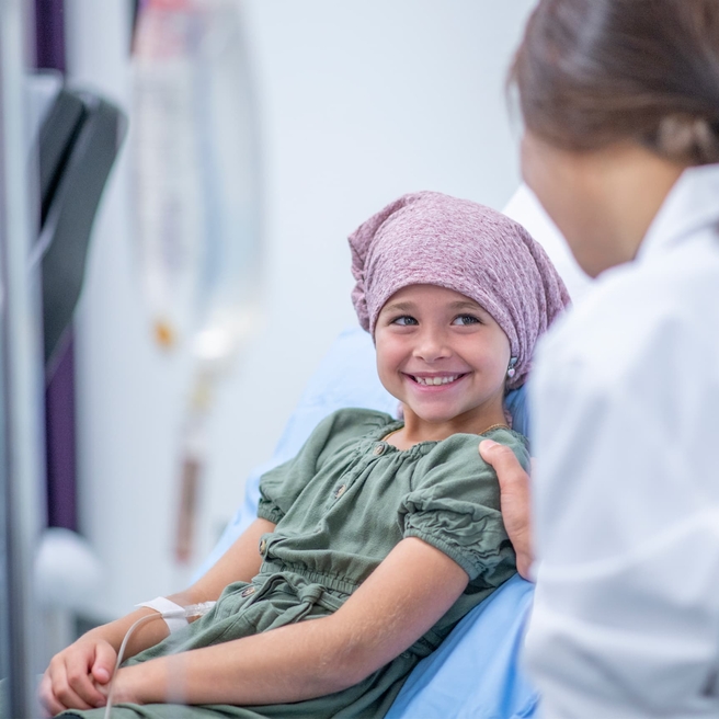 An elementary age girl talking to medical doctor wearing headscarf receiving infusion.