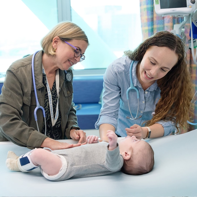 Two doctors examining baby patient in a hospital bed.