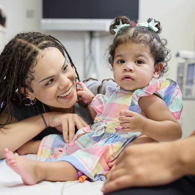 Mom smiling and looking at her little girl on exam table.