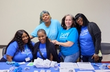 A small group of smiling Community Health Workers in blue t-shirts working at a community event.