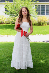Addison in a white dress holding flowers at her high school graduation.