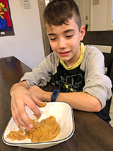 Dominic putting his hands into a plate of peanut butter