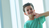 Young boy cancer patient sitting by window smiling
