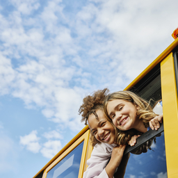 Smiling school age girls lean out of school bus windows