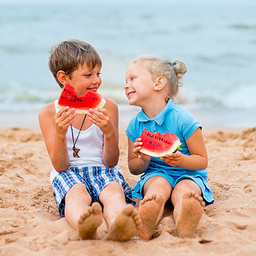 Two kids on the beach eating watermelon