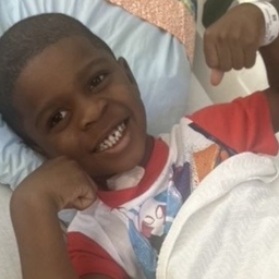Khymir flexing his arms and smiling in hospital bed