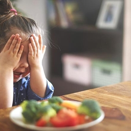 Young girl with hands over eyes sitting in front of a plate of food Young girl with hands over eyes sitting in front of a plate of food