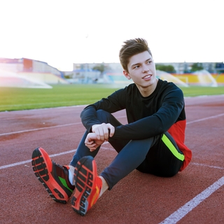 Older teen boy sitting on a track wearing cleats looking up.