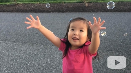 Avery extending her arms reaching for floating bubbles outside