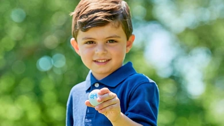 Young boy holding golf ball featuring CHOP logo